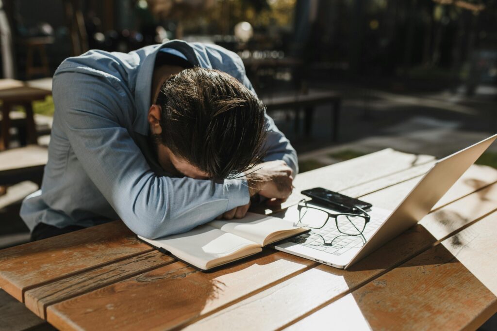 A man sits with his head resting on a laptop, appearing weary and discouraged. His posture suggests frustration or exhaustion.