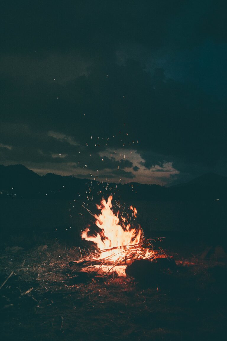 An outdoor fire pit surrounded by rustic stone, emanating a warm glow amidst the darkness of the night.